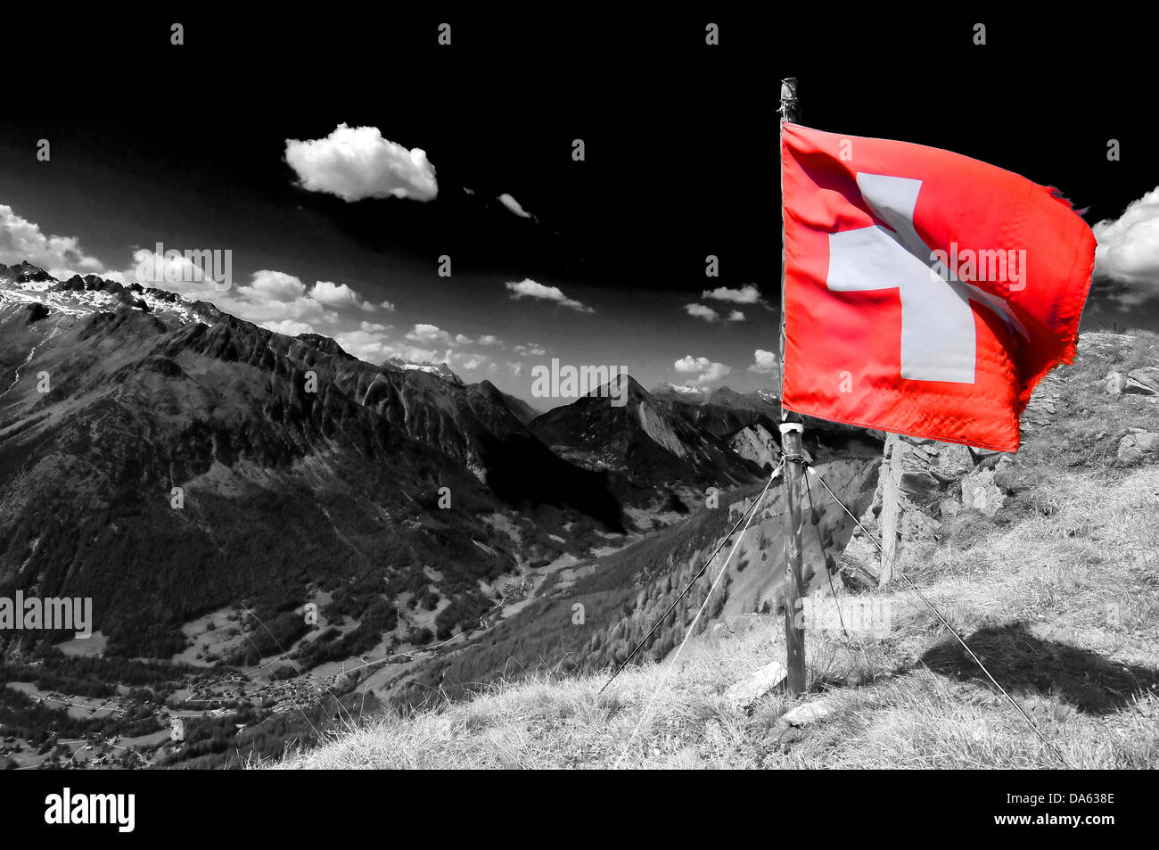 Una bandera suiza ondea desde la cima de una montaña en los alpes suizos, un valle con un pueblo suizo, en un bonito y soleado da Foto de stock