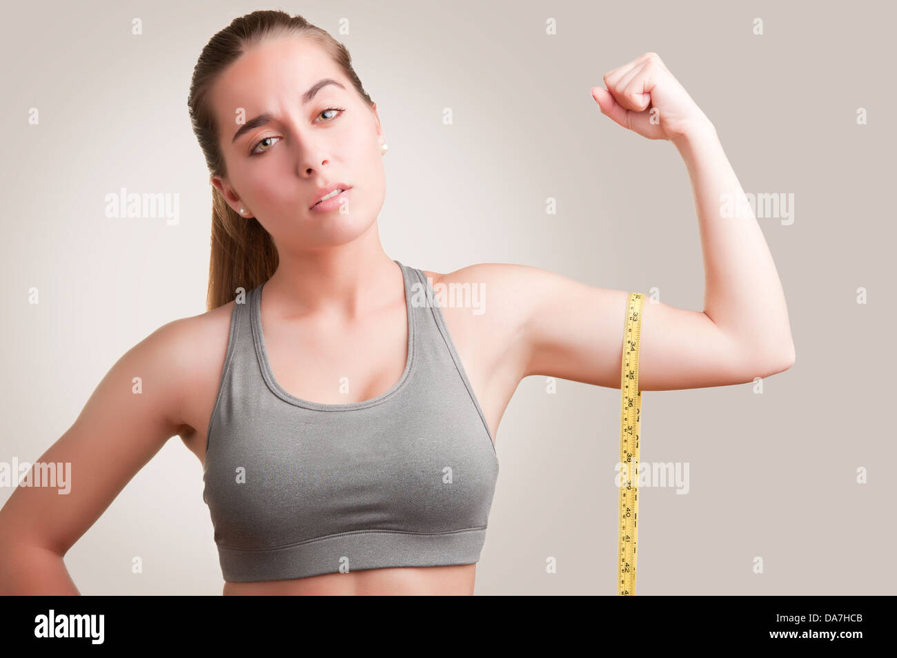 Mujer poderosa midiendo sus bíceps con una cinta de medición amarilla Foto de stock