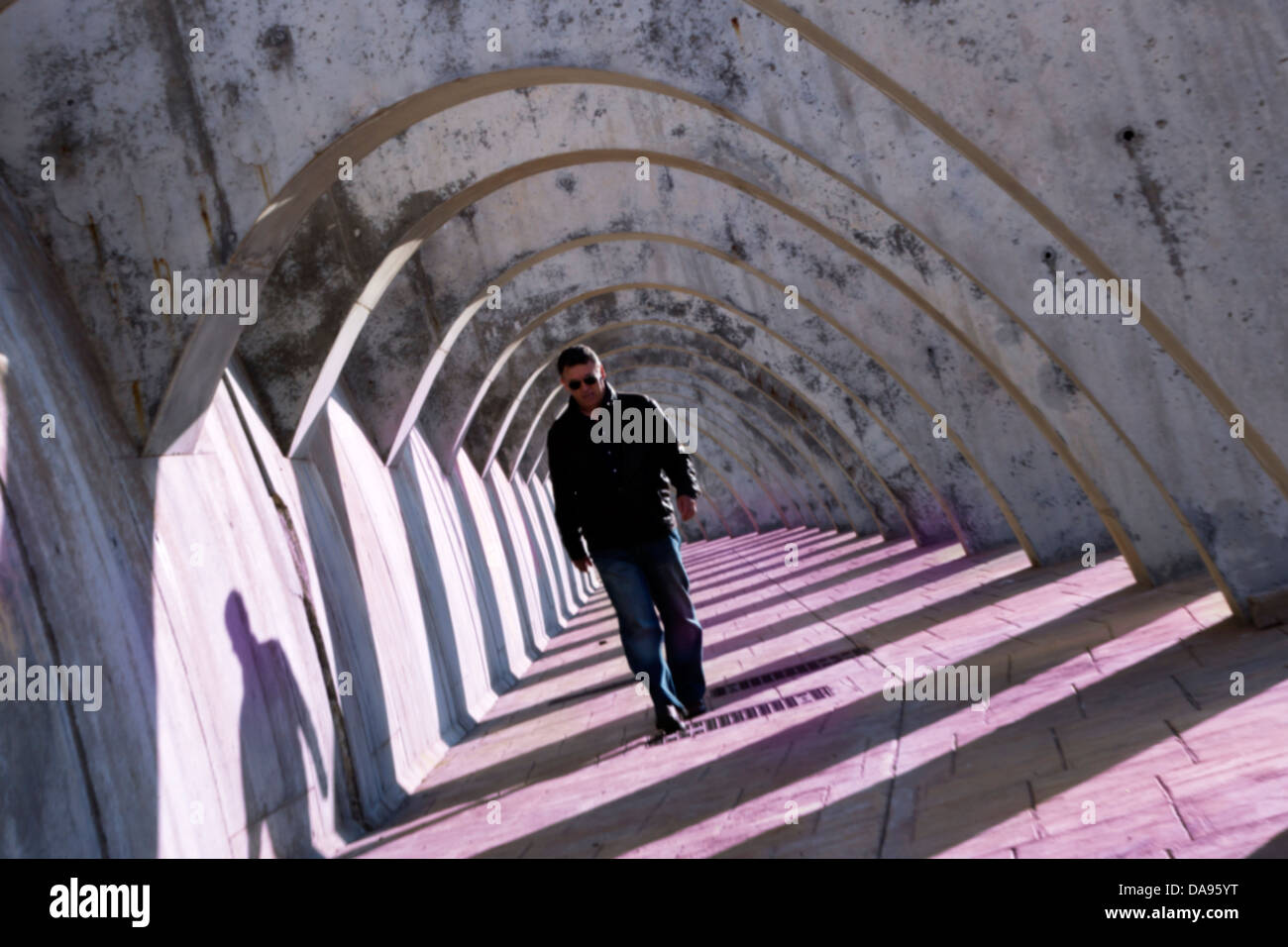 Misterioso hombre caminando bajo la pasarela arqueada. Foto de stock