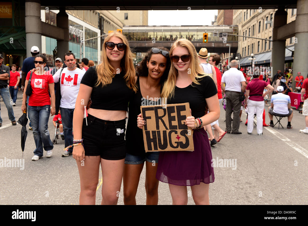 Tres chicas jóvenes ofrecen gratuitamente abrazos a la masiva concurrencia en Rideau Street en Ottawa, capital canadiense, durante el Día de Canadá. Foto de stock