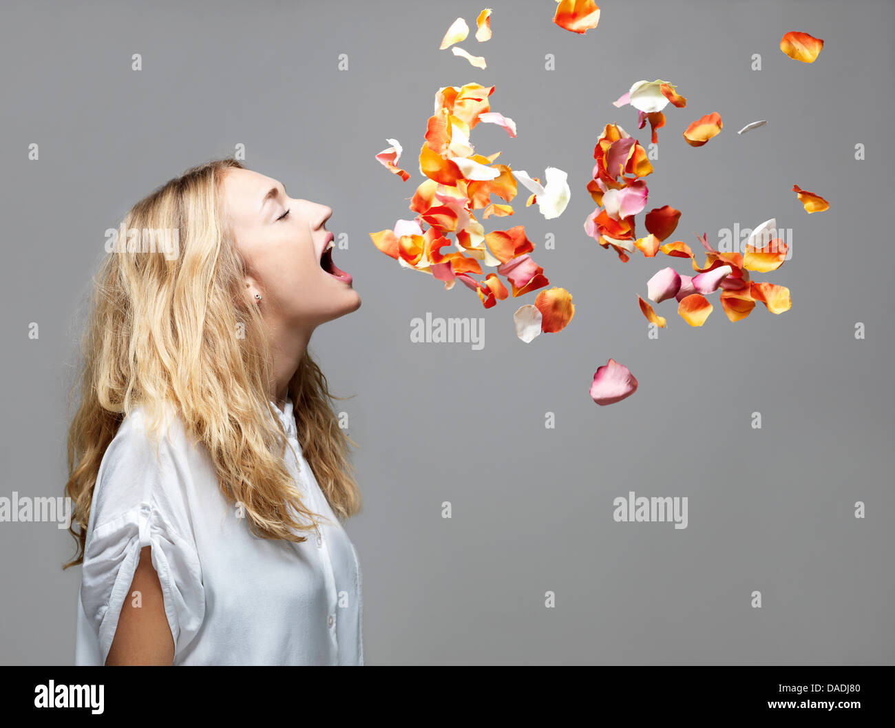 Mujer joven con la boca abierta un pétalos flotando en el aire. Foto de stock