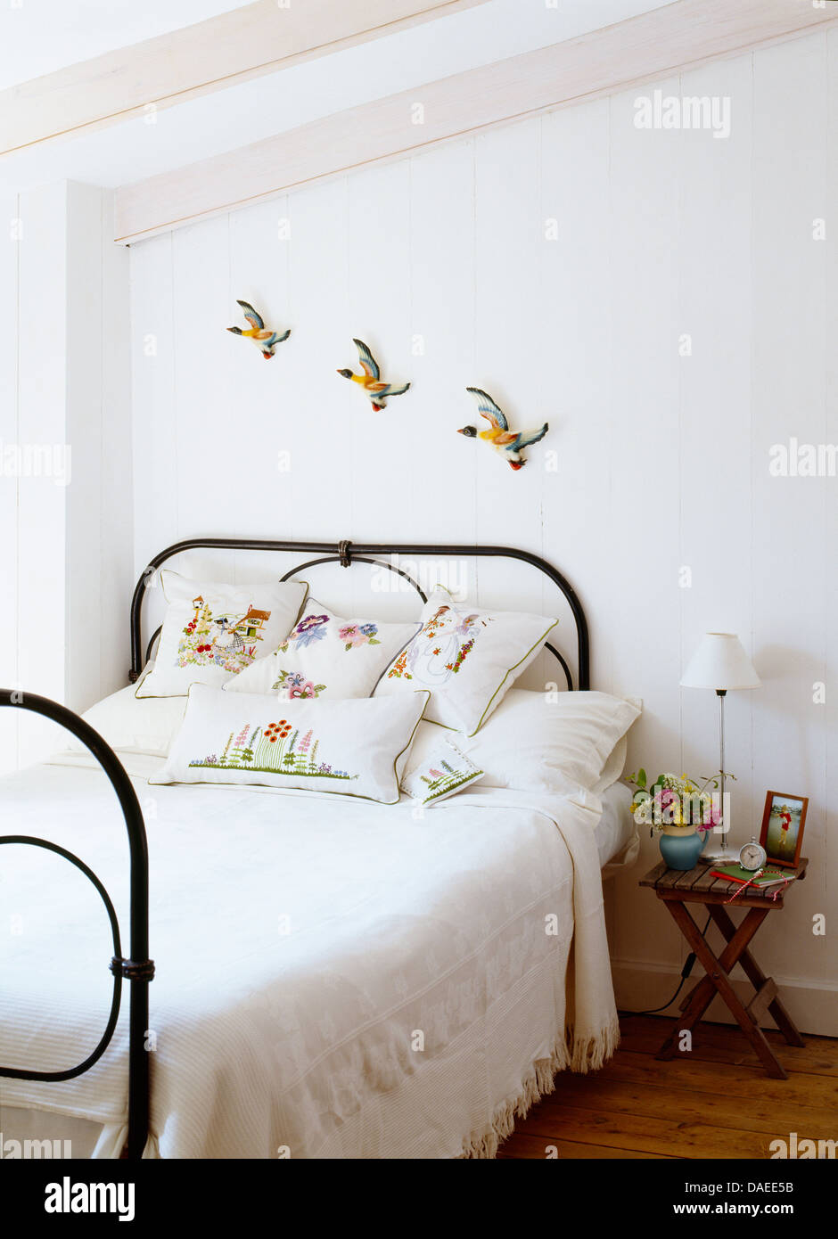 Alfarería patos volando en pared sobre la cama de hierro forjado de  cubierta con ropa de cama blanca y cojines bordados en blanco dormitorio  costera Fotografía de stock - Alamy