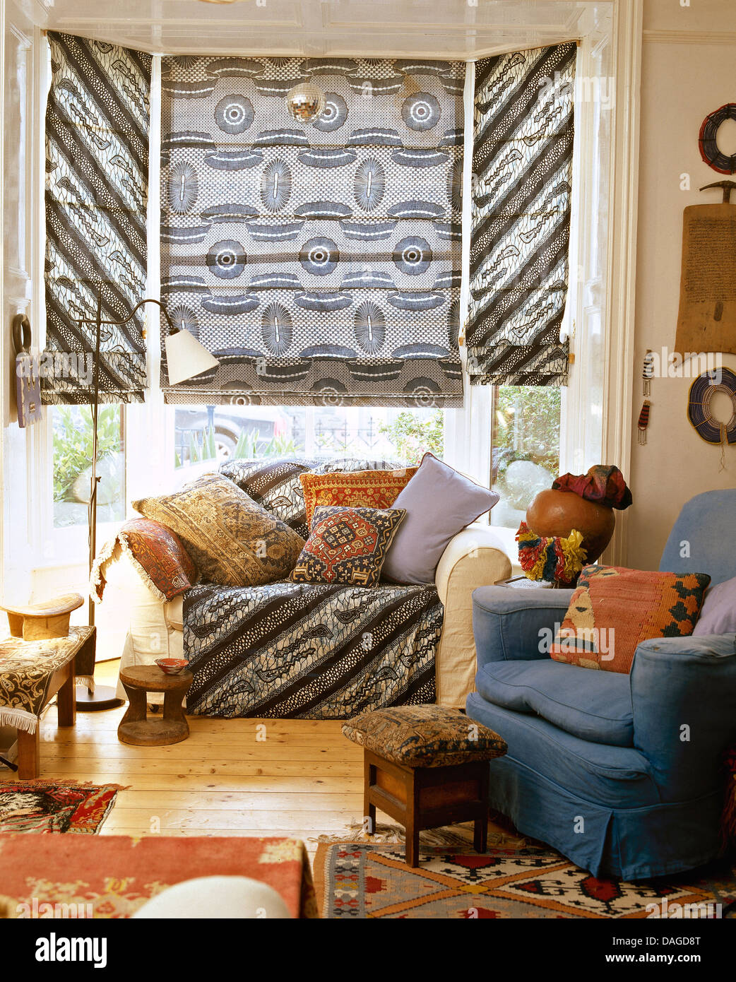 Telas grises ciego romano en bahía ventana encima de un sofá con cojines  apilados en la sala de estar con sillones azules y alfombras étnicas  Fotografía de stock - Alamy