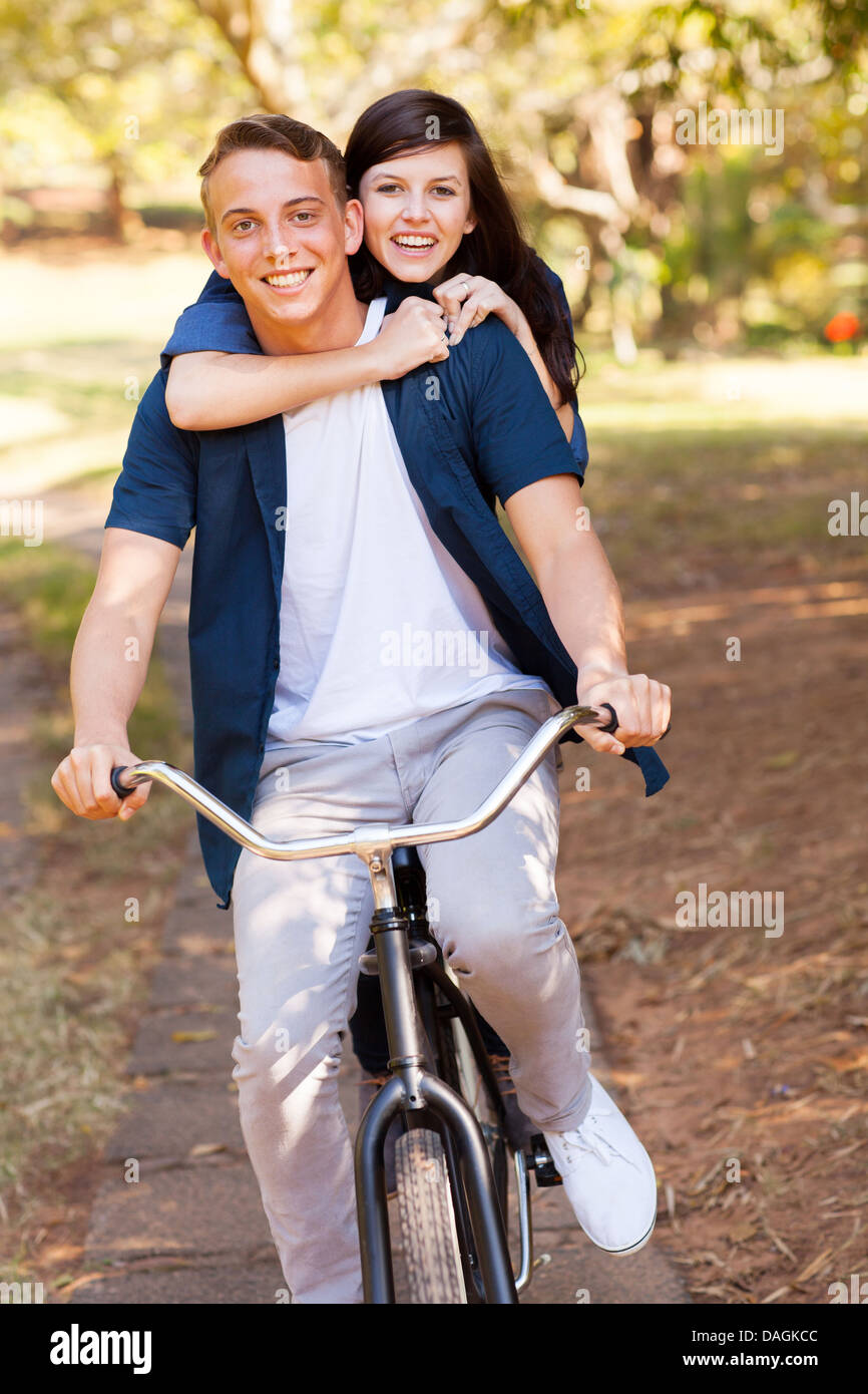 Alegre pareja de adolescentes divirtiéndose en bicicleta en el parque Foto de stock