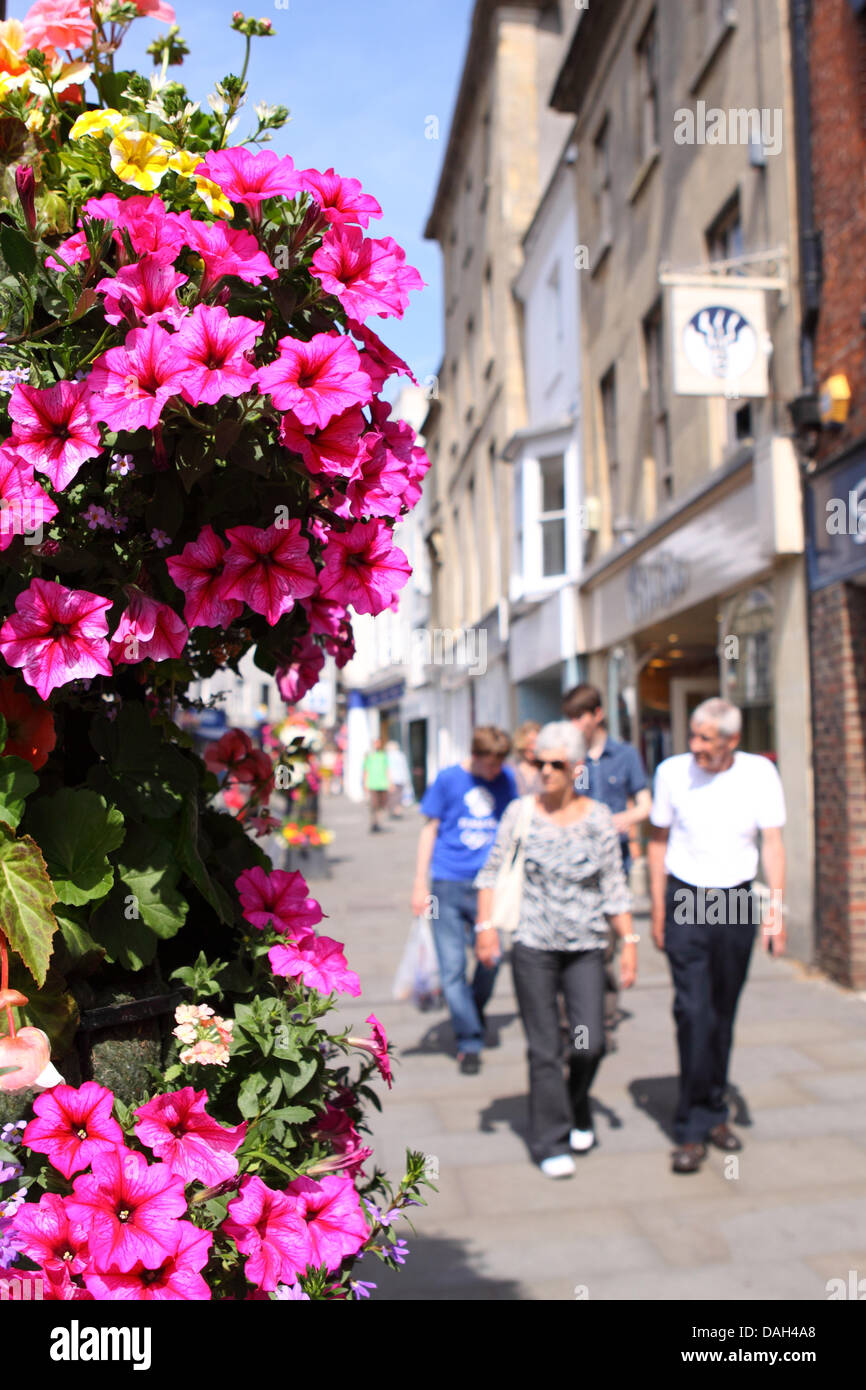 Wells Somerset colgaderas coloridas flores a lo largo de High Street con los compradores y visitantes Foto de stock