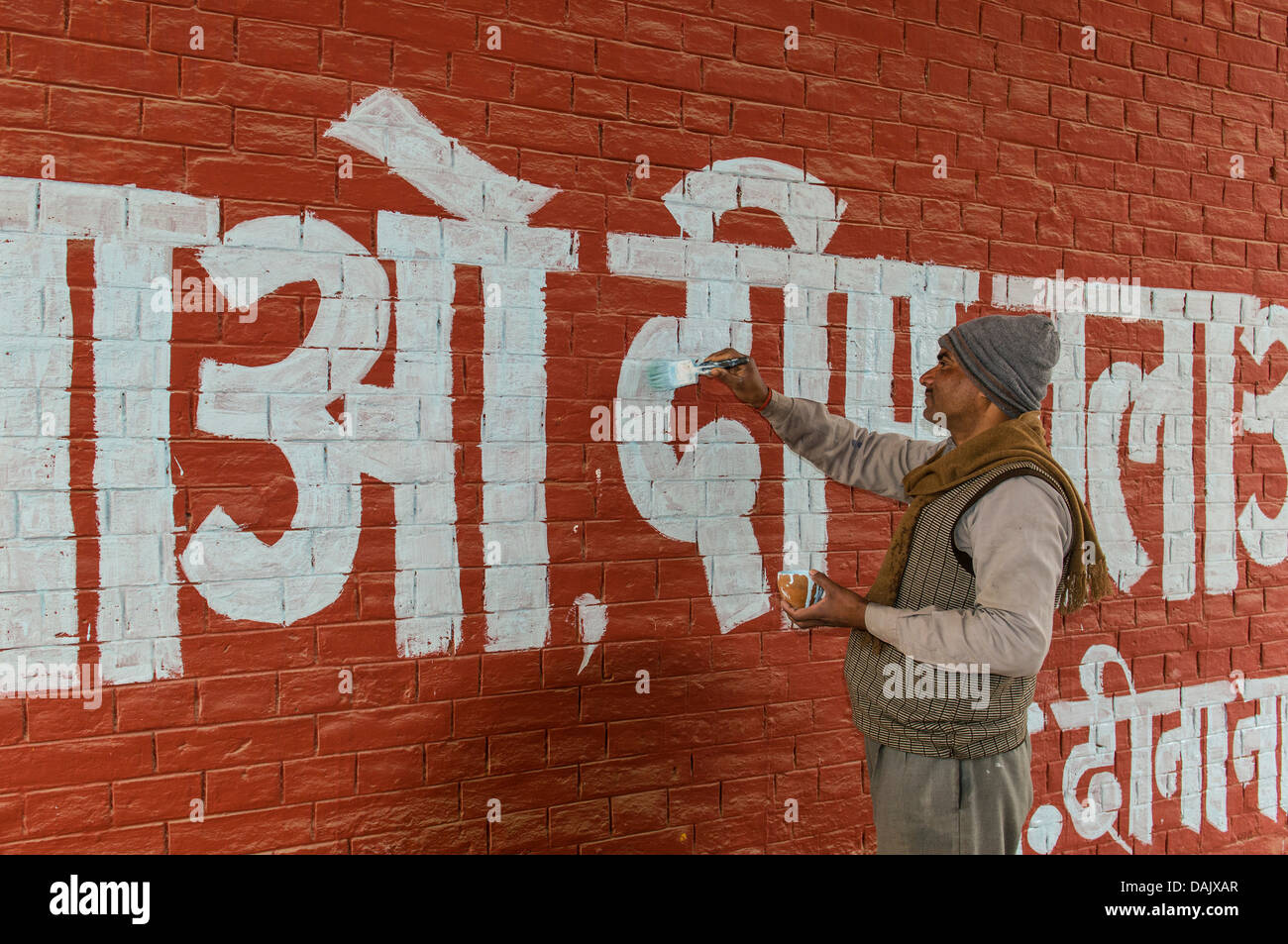 Pintura de hombre de letras blancas en lengua hindi en una pared roja Foto de stock