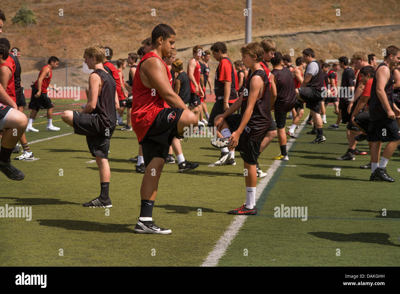 Escuela multiétnica atletas calientan con ejercicios de flexibilidad ya que comienzan la práctica de fútbol de primavera en California. Foto de stock
