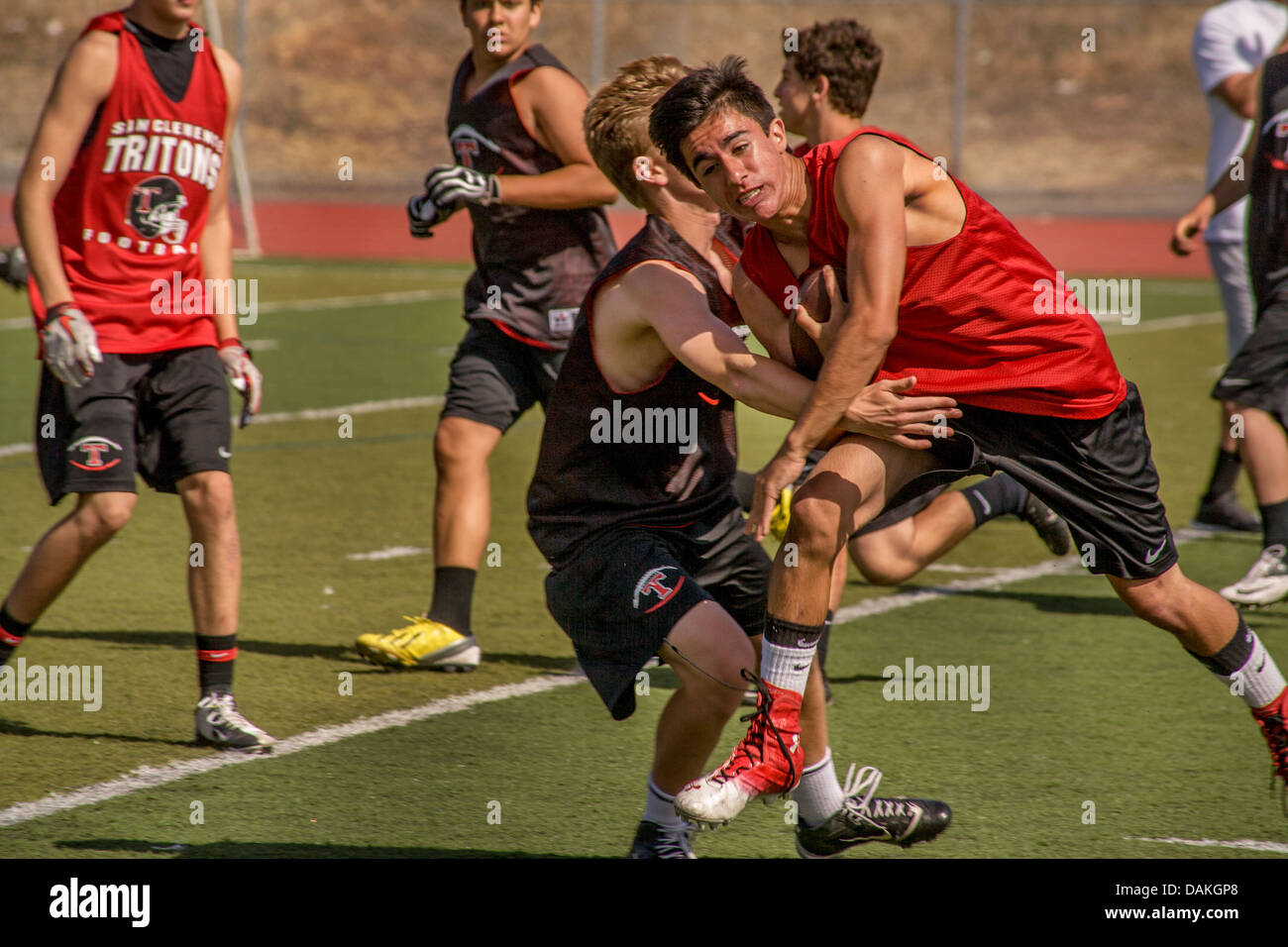 Llevando la pelota, un colegio atleta esquiva tacklers mientras se ejecuta durante la práctica de fútbol de primavera en San Clemente, CA. Foto de stock