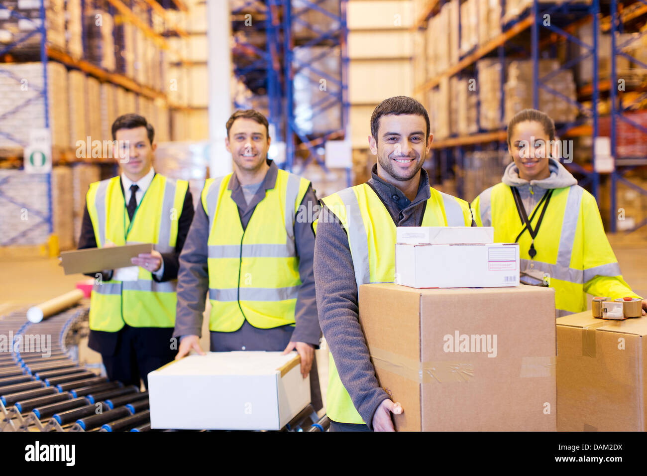 Los trabajadores sonriendo por banda transportadora en el almacén Foto de stock