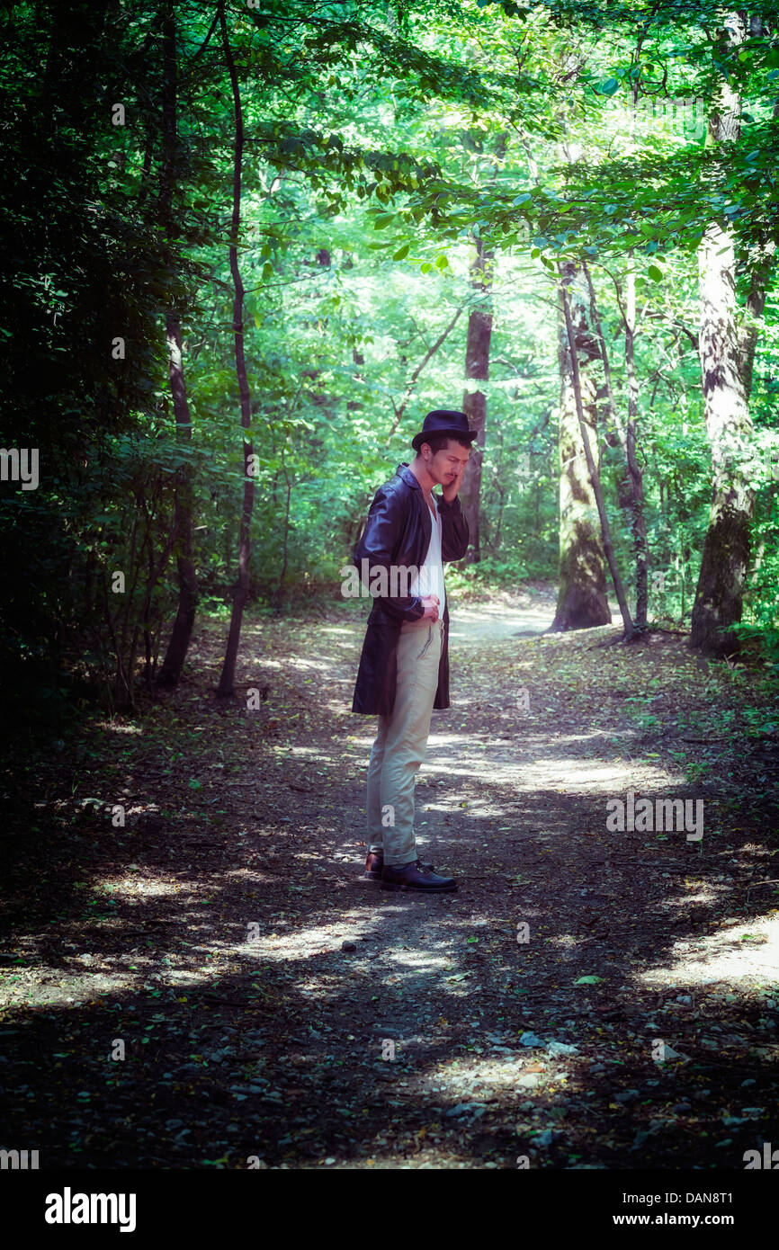 Agotado hombre con chaqueta negra y sombrero en el bosque Foto de stock