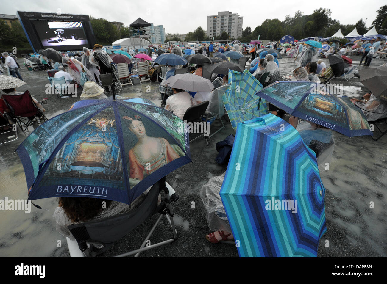 Wagner fans valiente la repentina cloudburst con ponchos de lluvia y  Paraguas durante el evento de visualización pública de Wagner de la ópera  "Lohengrin" en el Volksfestplatz (Folk Festival Plaza) en Bayreuth,