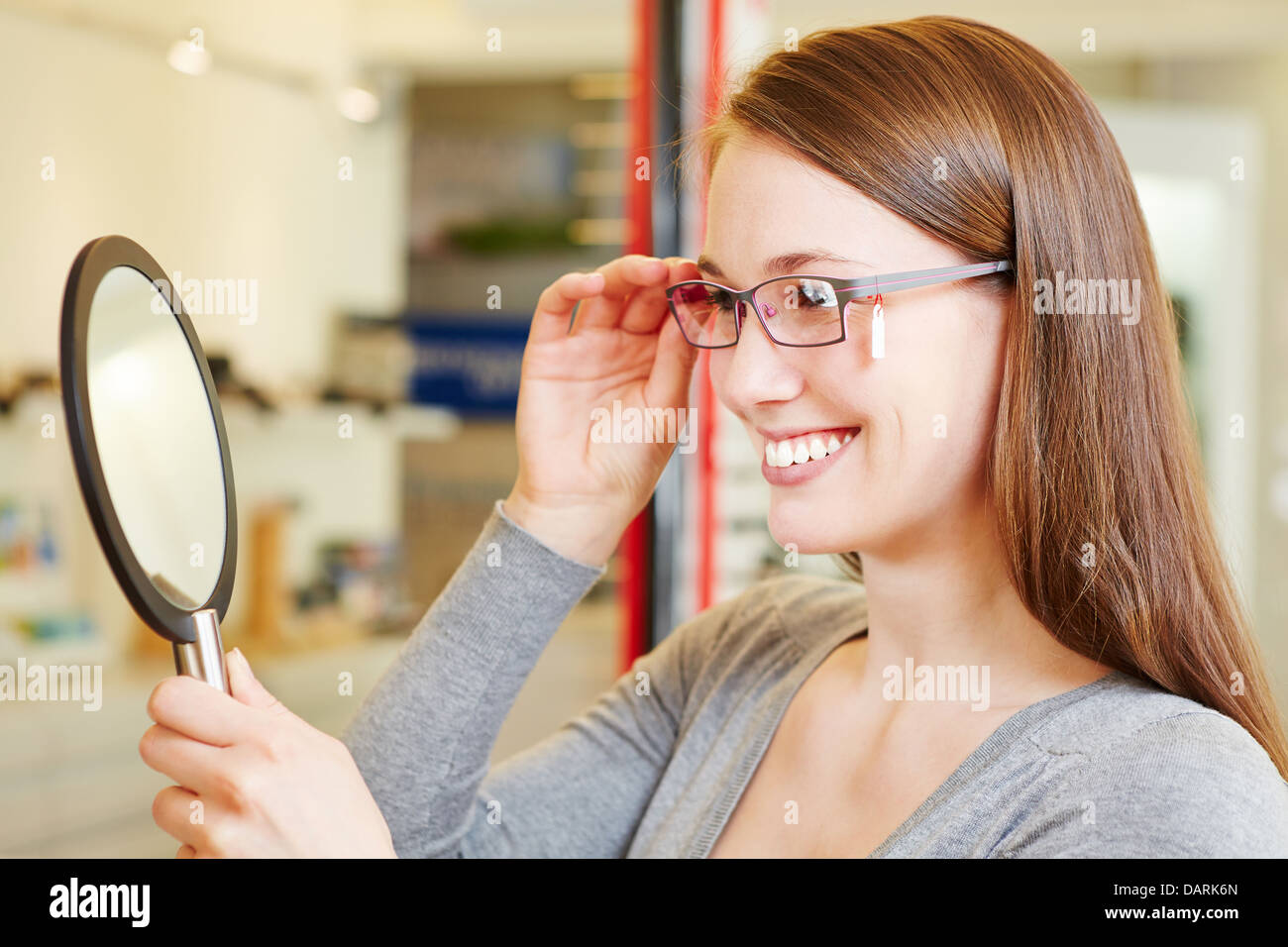 Mujer joven de revisar sus nuevas gafas en un espejo óptico en la tienda minorista Foto de stock