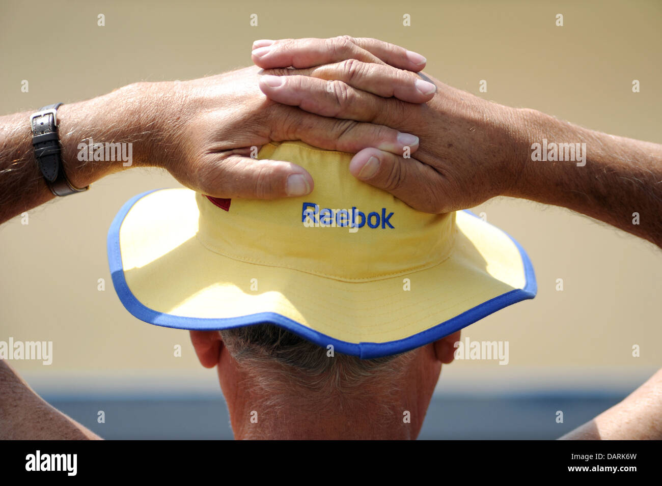 Hombre vestido con ropa deportiva Reebok sombrero para el sol con las manos detrás de la cabeza en clima caluroso Foto de stock