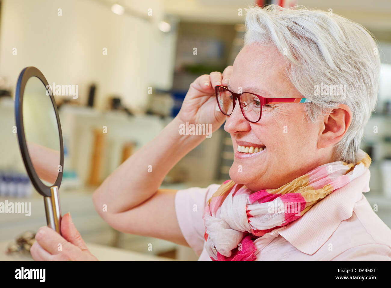 Feliz anciana con gafas nuevas mirarse a un espejo en el almacén óptico Foto de stock