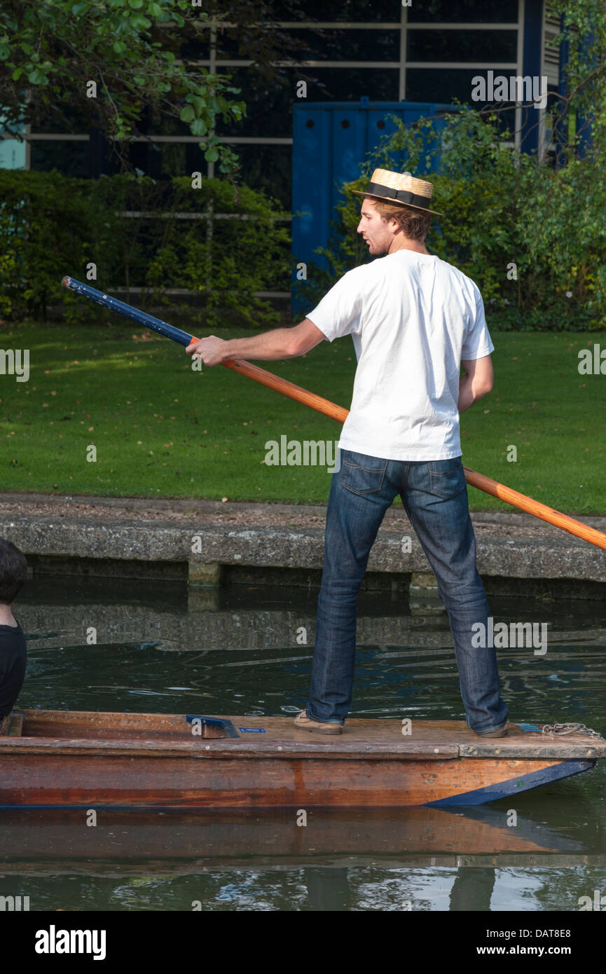 Un hombre joven de pie en la parte de atrás de un punt sosteniendo un punt pole remar en Cambridge llevar sombrero paja navegante Foto de stock