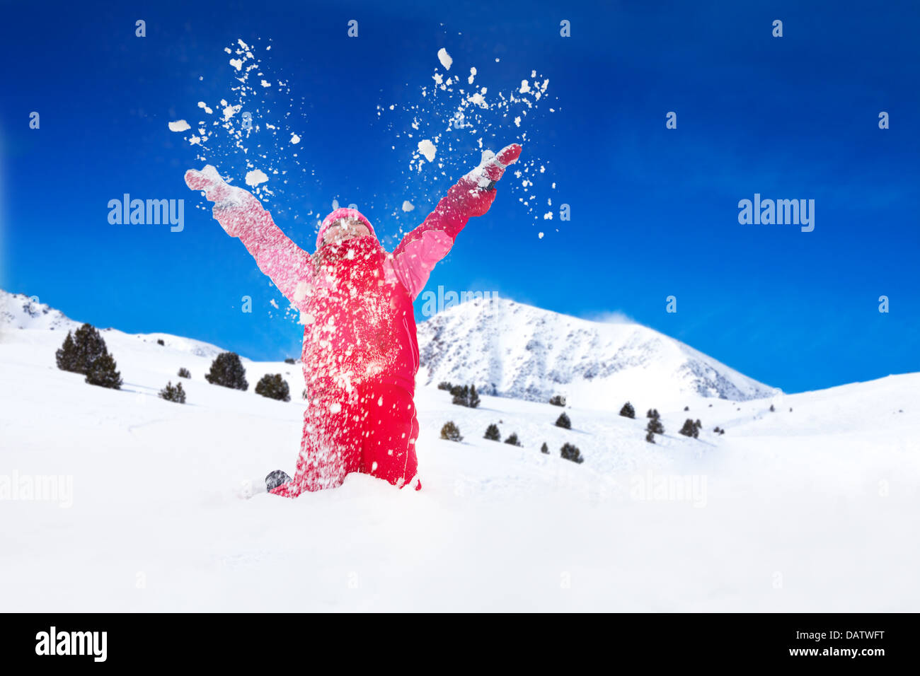 Poco feliz chica sonriente arroja nieve en el aire con copos de nieve volando en todas direcciones Foto de stock