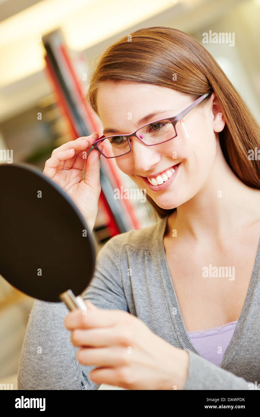 Feliz mujer sonriente con gafas nuevas mirando en el espejo a óptico Foto de stock