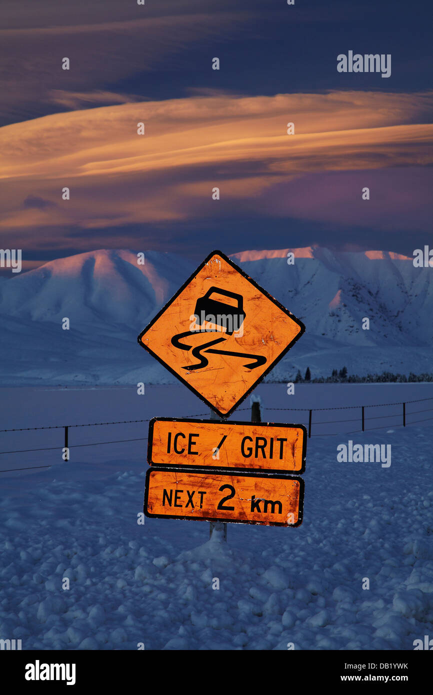 La señal de advertencia y carreteras heladas en alpenglow Hawkdun Rango y nubes lenticulares, Maniototo, Central Otago, Isla del Sur, Nueva Zelanda Foto de stock