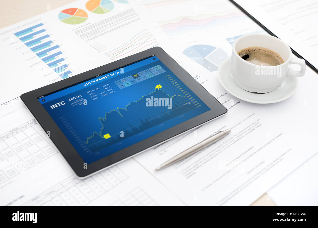 Tableta digital moderna con aplicación de datos bursátiles en un escritorio con algunos papeles y documentos, pluma y una taza de café Foto de stock