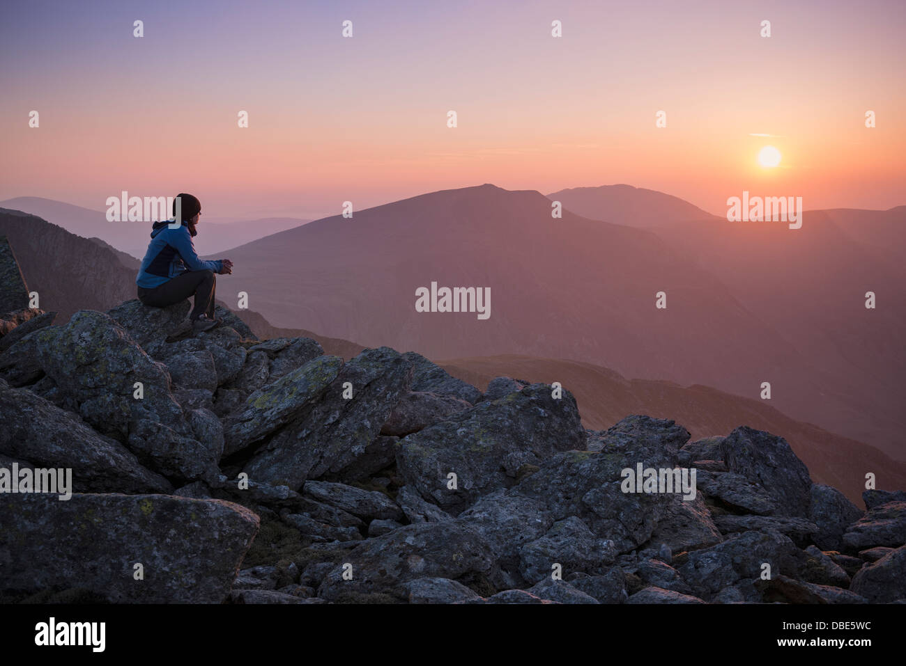 Excursionista hembra vigila la puesta de sol sobre las montañas de cumbre de Glyder Fach, el parque nacional de Snowdonia, Gales Foto de stock