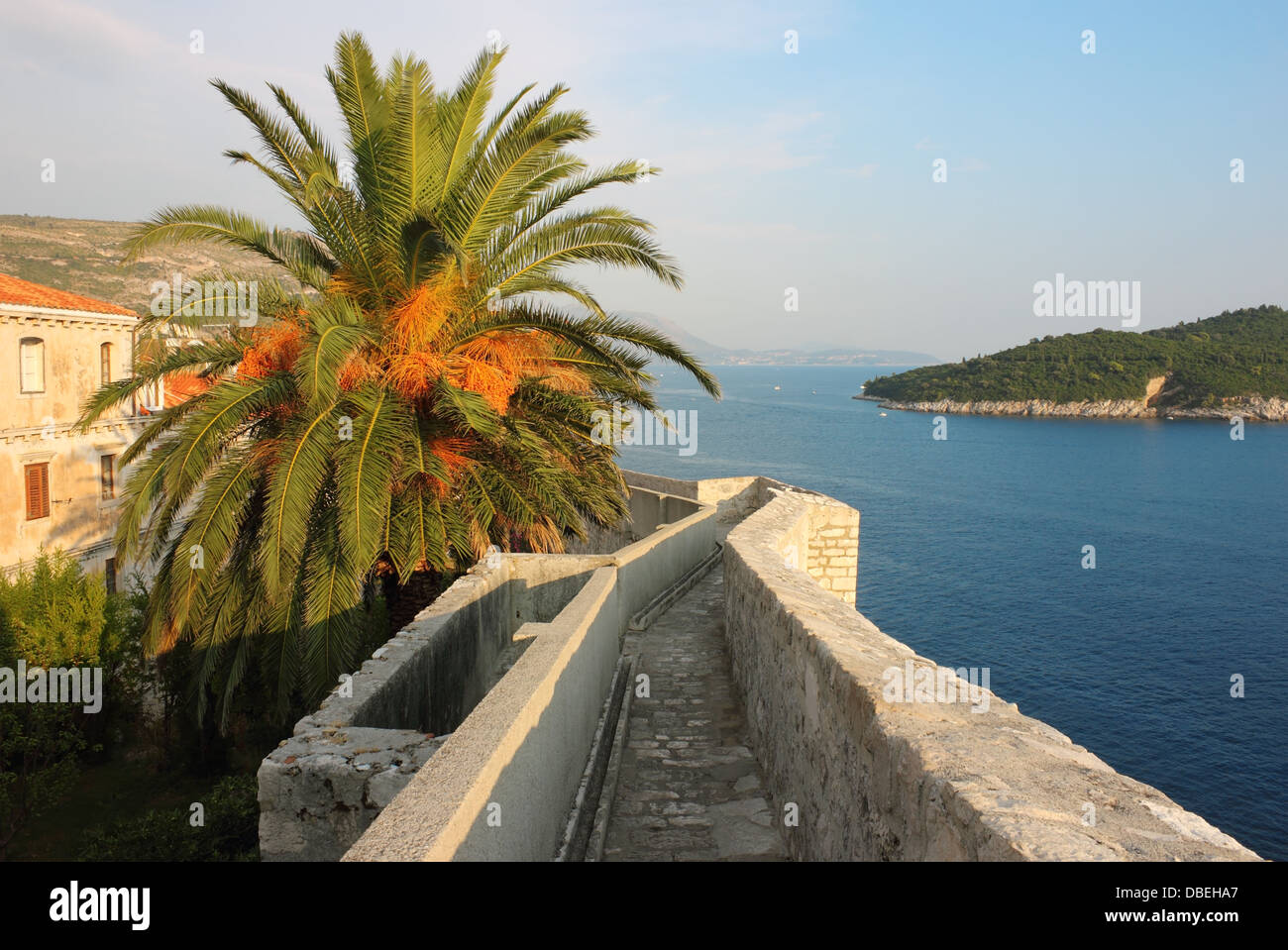 Caminar alrededor de la muralla fortificada de Dubrovnik, con una vista hacia Isla Lokrum en la cálida luz del atardecer. Foto de stock
