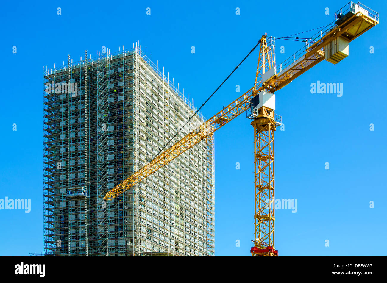 Sitio de construcción de un gran edificio cubierto de andamios, marco enorme grúa en el lugar de trabajo. Foto de stock