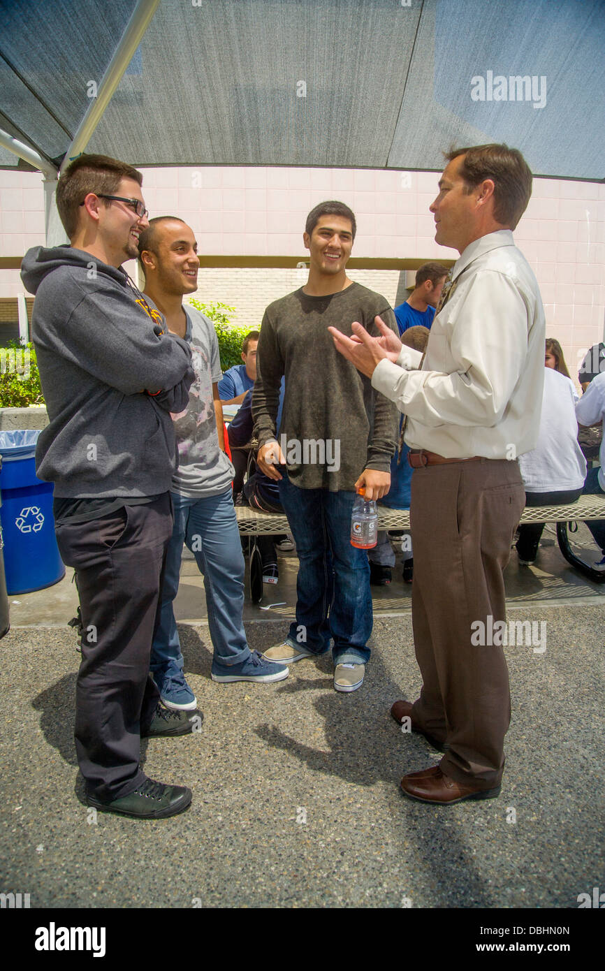 Un director de una escuela secundaria conversaciones con tres varones estudiantes superiores en el campus suburbano al mediodía en Aliso Viejo, CA. Foto de stock
