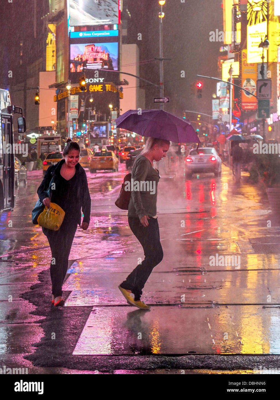 Dos mujeres afroamericanas cruzar Broadway en Times Square, en Nueva York, en una noche lluviosa. Nota carteles publicitarios luminosos. Foto de stock