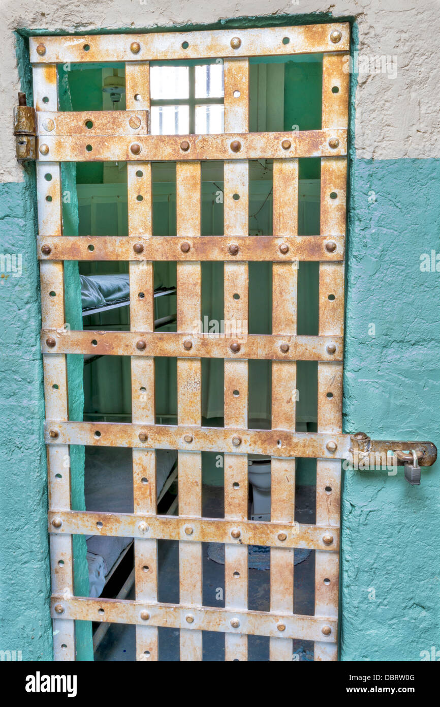 Robar barras en la puerta de una celda de la prisión con una cama Foto de stock