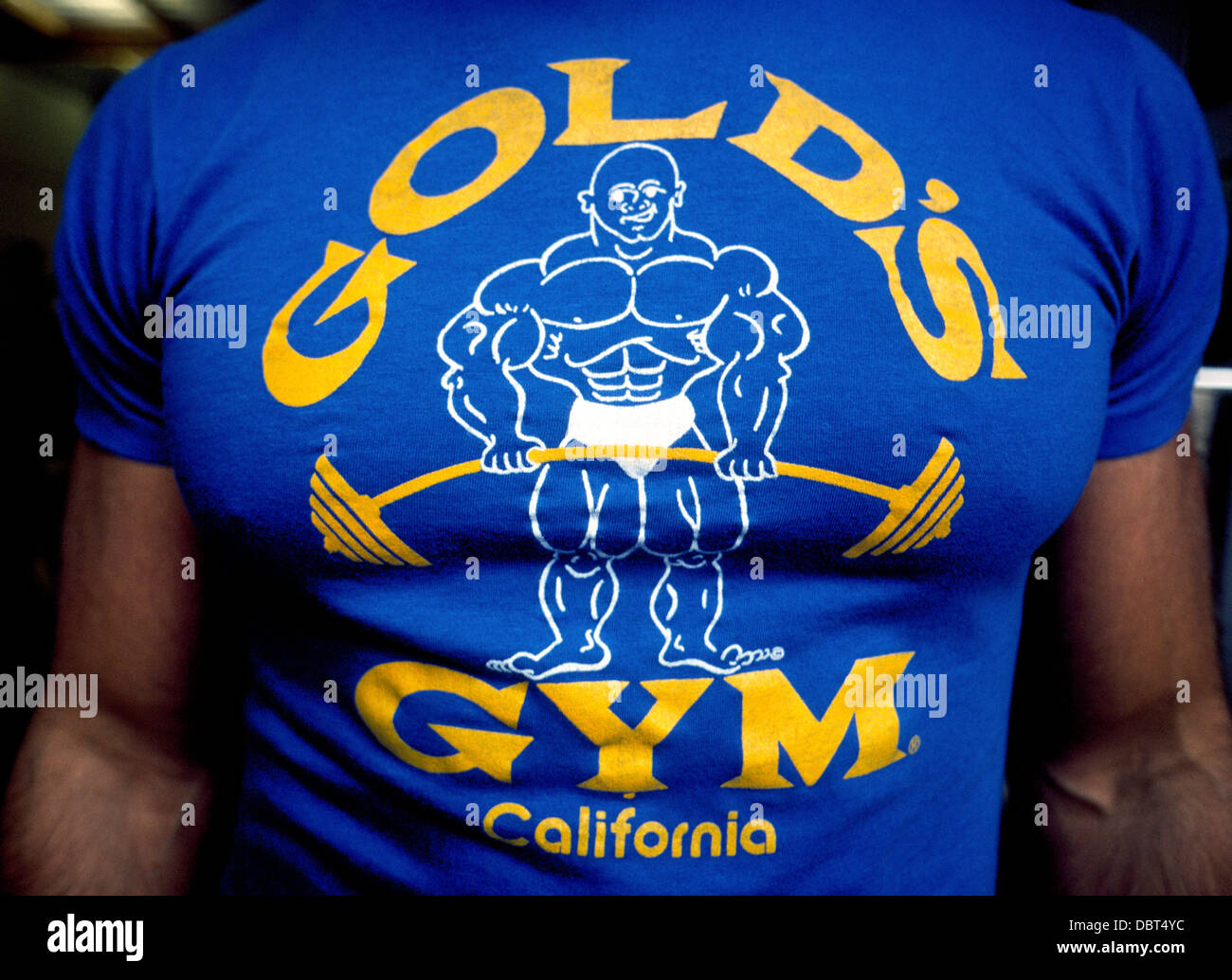Un músculo hombre viste una camiseta con el logotipo de Gold's Gym Fitness  Centers en todo el mundo, establecido en 1965 por Joe Oro en Venice Beach,  California, Estados Unidos Fotografía de