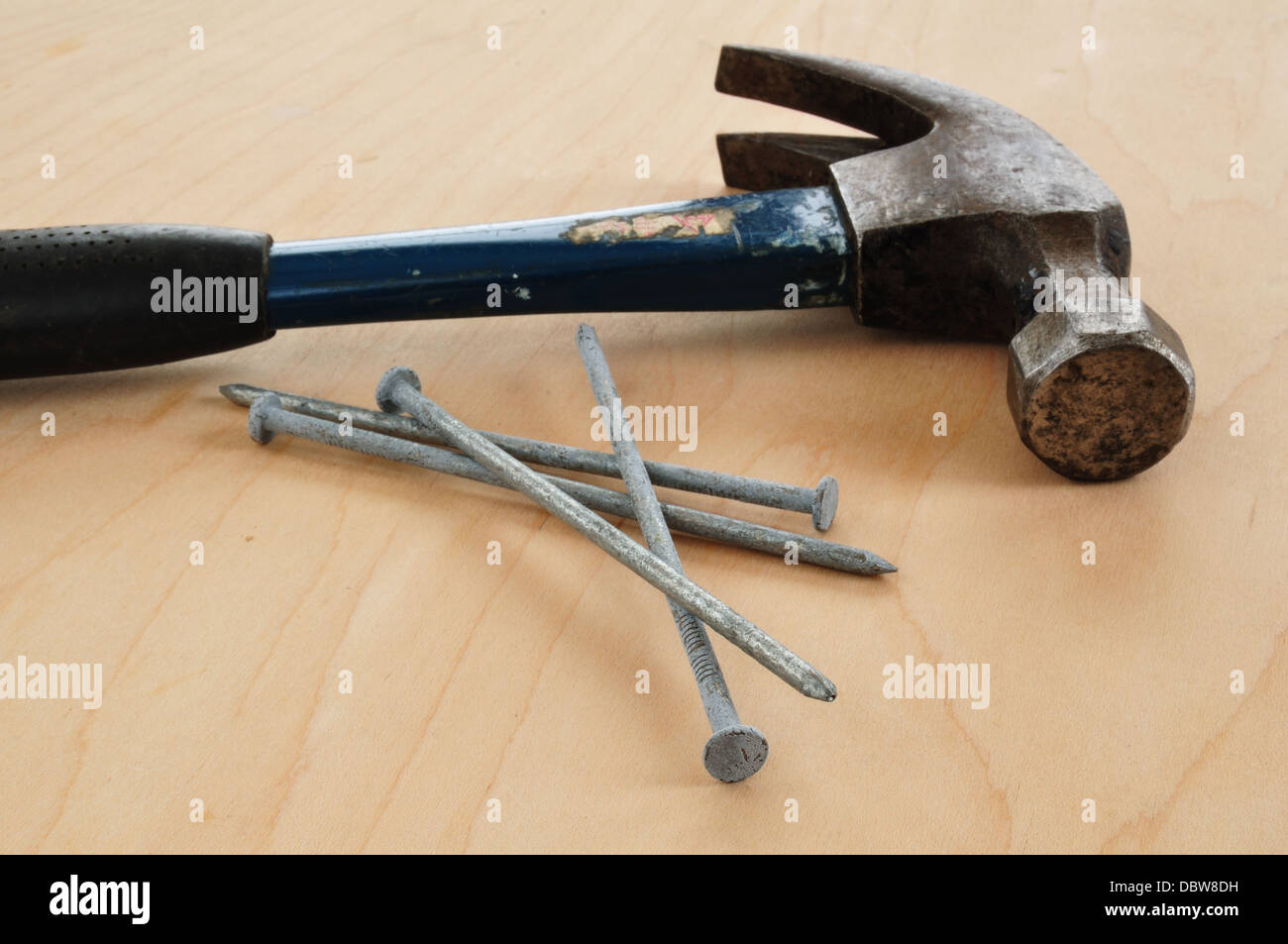 Clavos galvanizados y un martillo de orejas sobre una tabla de madera Foto de stock