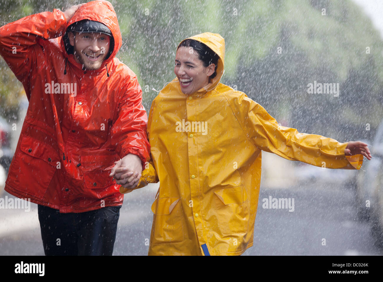 Feliz pareja tomados de la mano y corriendo en la calle lluviosa Foto de stock