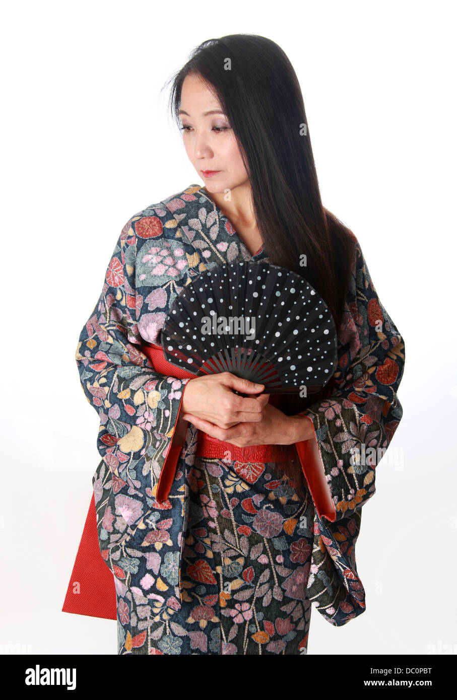 Dama japonesa sentada en el suelo vistiendo un tradicional Kimono telas azules y rojas y la celebración de un ventilador Foto de stock