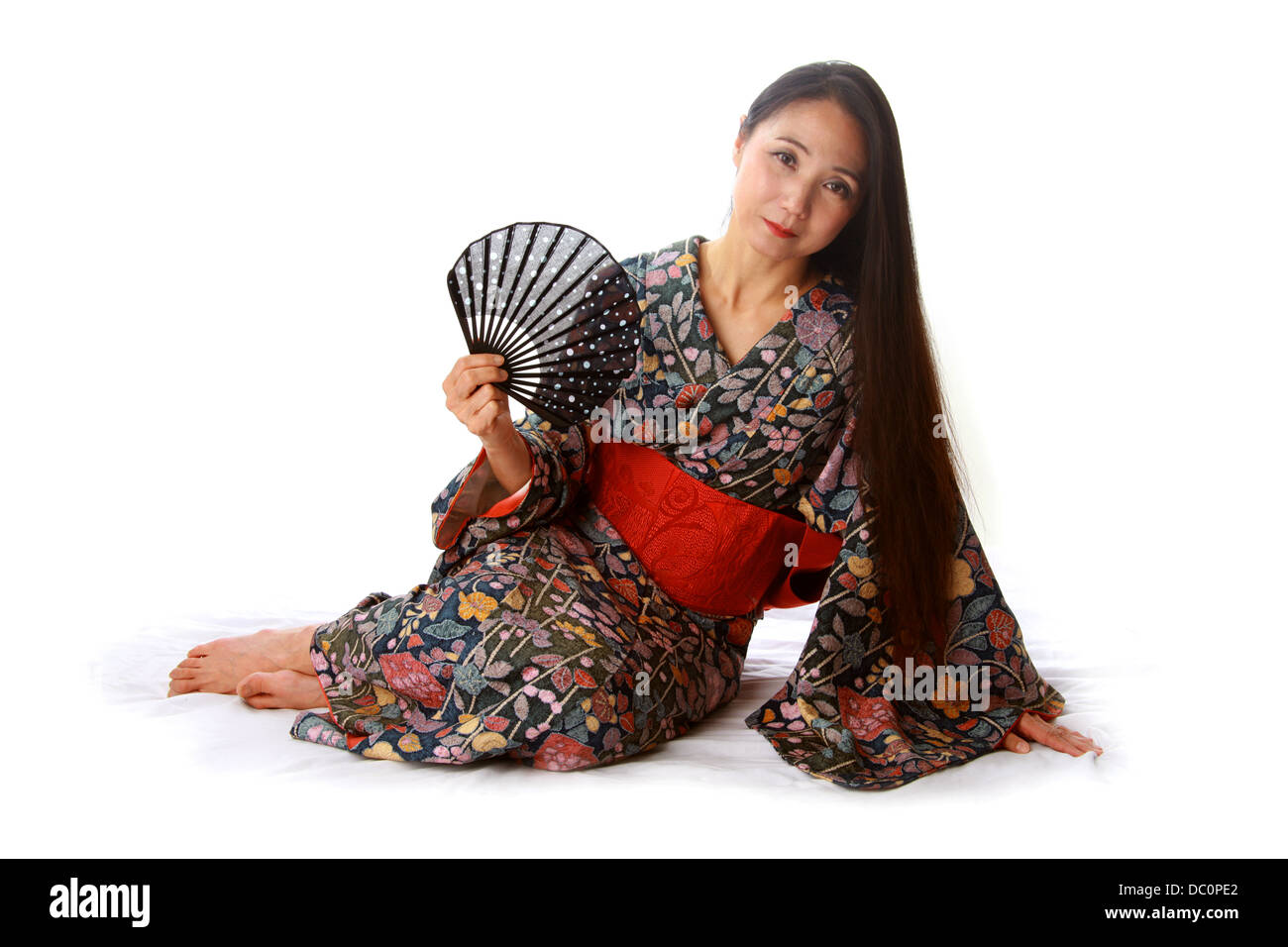 Dama japonesa sentada en el suelo vistiendo un tradicional Kimono telas azules y rojas y la celebración de un ventilador Foto de stock