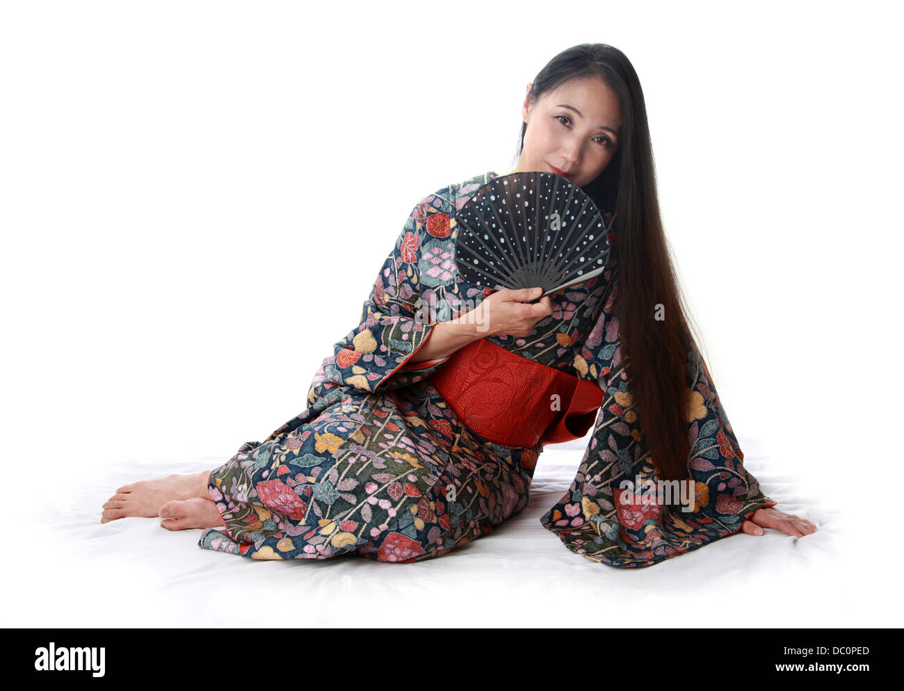Dama japonesa sentada en el suelo vistiendo un tradicional Kimono telas azules y rojas y la celebración de un ventilador Foto de stock