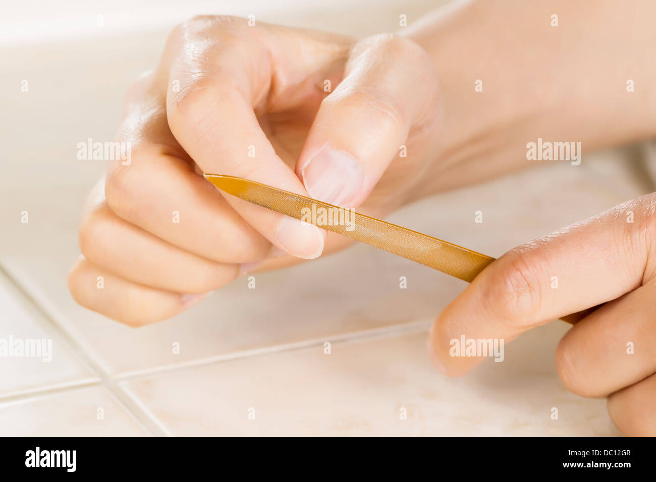 Cerrar la foto en horizontal de manos femeninas con lima de uñas de metal dorado en la parte delantera de herramienta Foto de stock