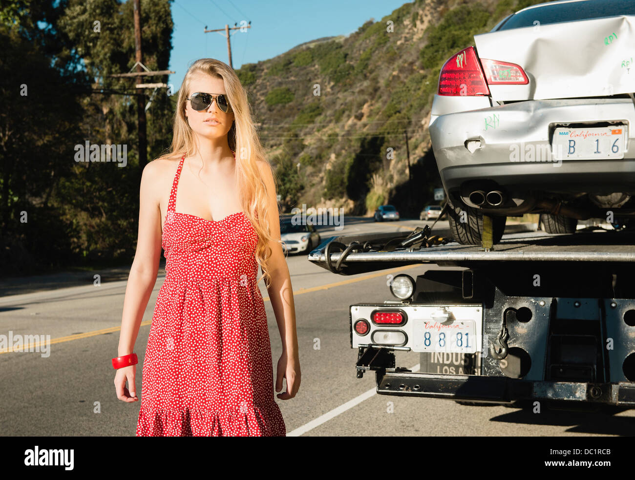 Mujer joven mirando a la cámara como Tow Truck quita auto dañado Foto de stock
