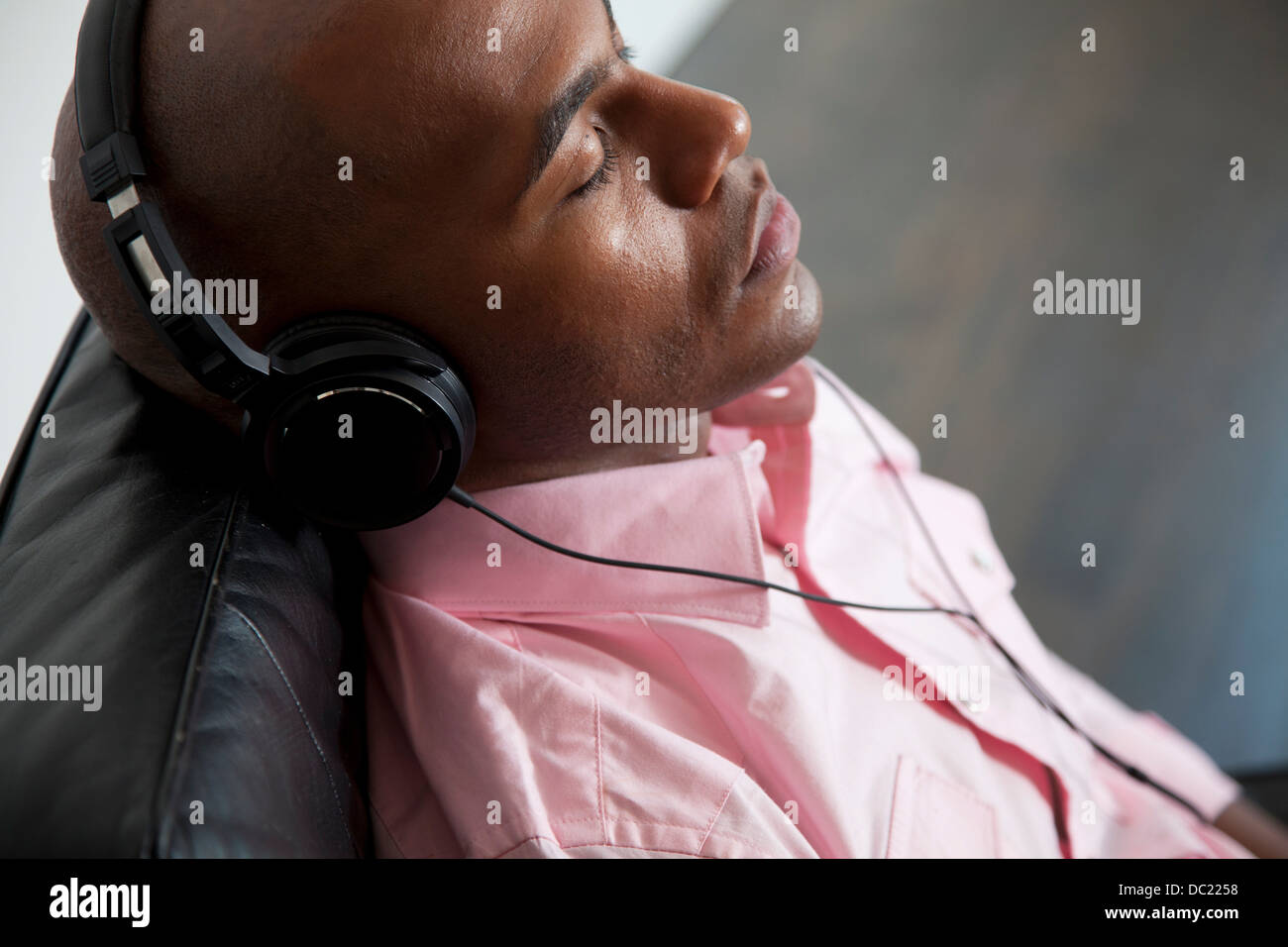Mitad hombre adulto escuchar auriculares sobre el sofá, los ojos cerrados Foto de stock