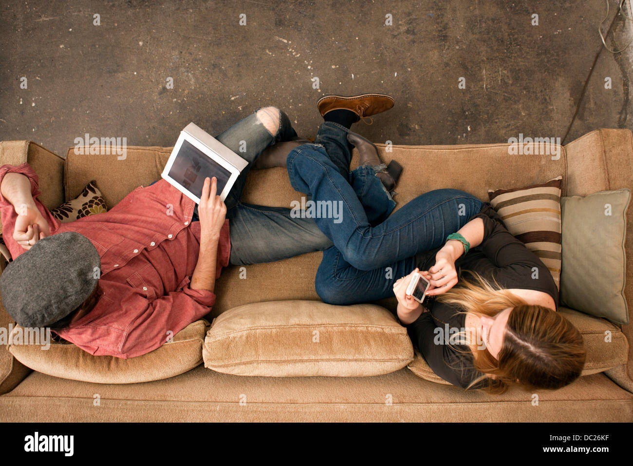 Pareja sentada en un sofá con digital tablet y smartphone Foto de stock