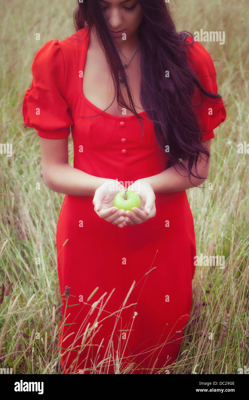 Una mujer en un vestido rojo, sosteniendo una manzana verde Foto de stock