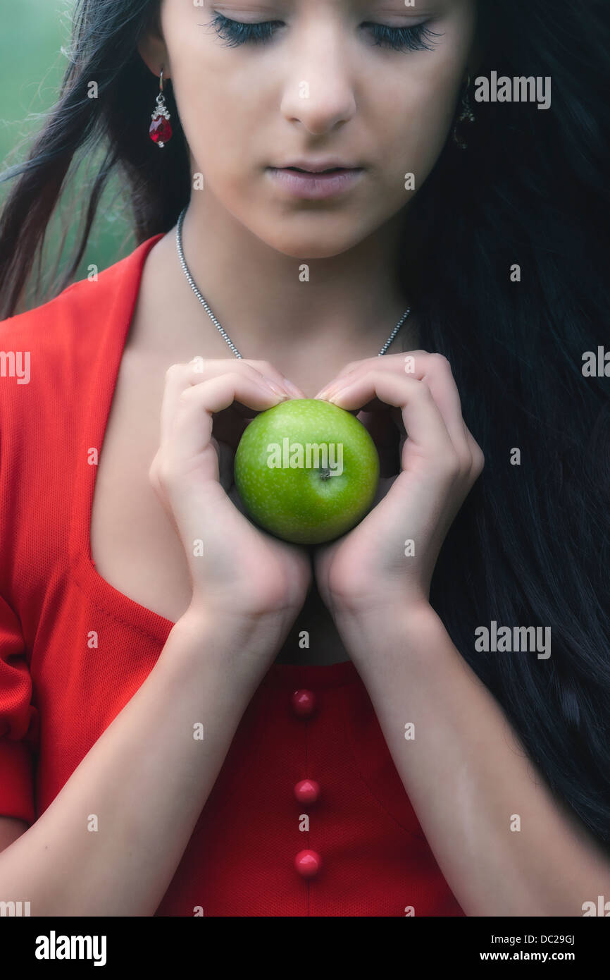 Una mujer en un vestido rojo, sosteniendo una manzana verde Foto de stock