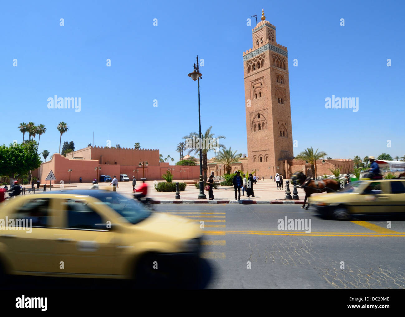 La mezquita Koutoubia o Mezquita Kutubiyya Marrakech Marruecos con un primer plano de la escena de la calle concurrida con taxis, vehículos y personas Foto de stock
