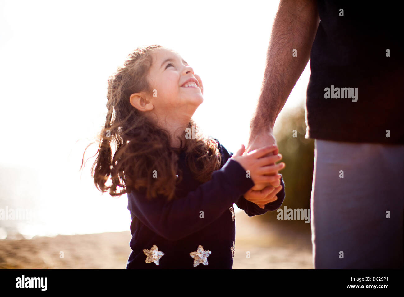 Chica sujetando la mano del padre, mirando hacia arriba Foto de stock