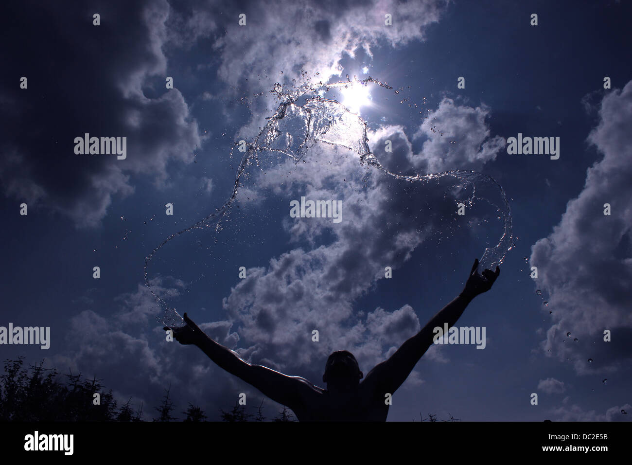 Hombre echándole agua en el aire, con sol y cielo azul antecedentes Foto de stock