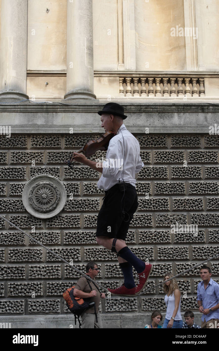 Hombre caminando en cuerda floja mientras toca violín, busker / Street Entertainer en el centro de la ciudad de Bath, Inglaterra Foto de stock