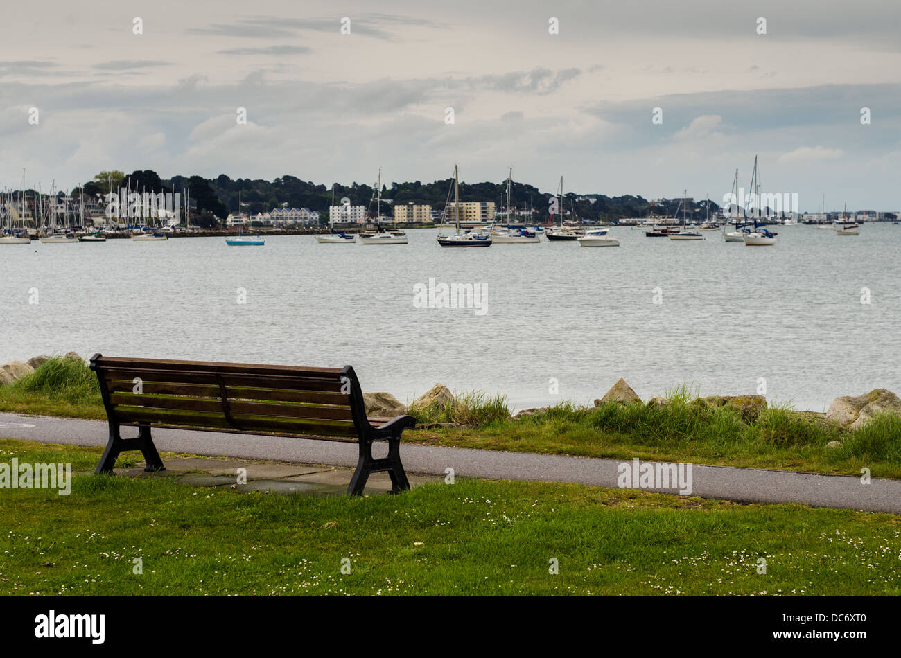 Un solitario en una banqueta vacía Seaside Park a orillas del Poole Harbour con yates anclados en la distancia. Foto de stock