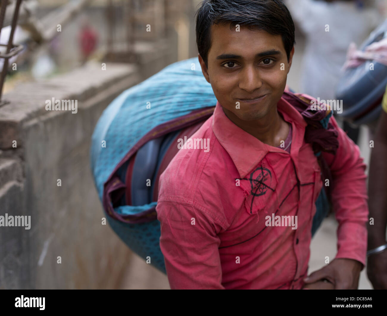 Joven hombre indio que transportaban mercancías en un chal sobre la calle en Varanasi, India Foto de stock
