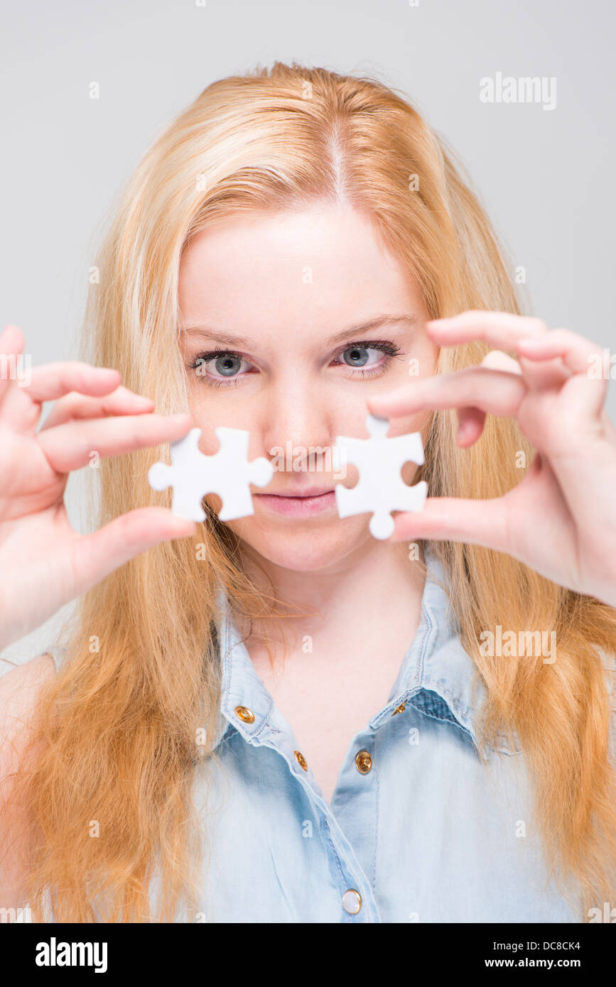 Joven Mujer rubia holding y examinar dos piezas de un rompecabezas blanco Foto de stock