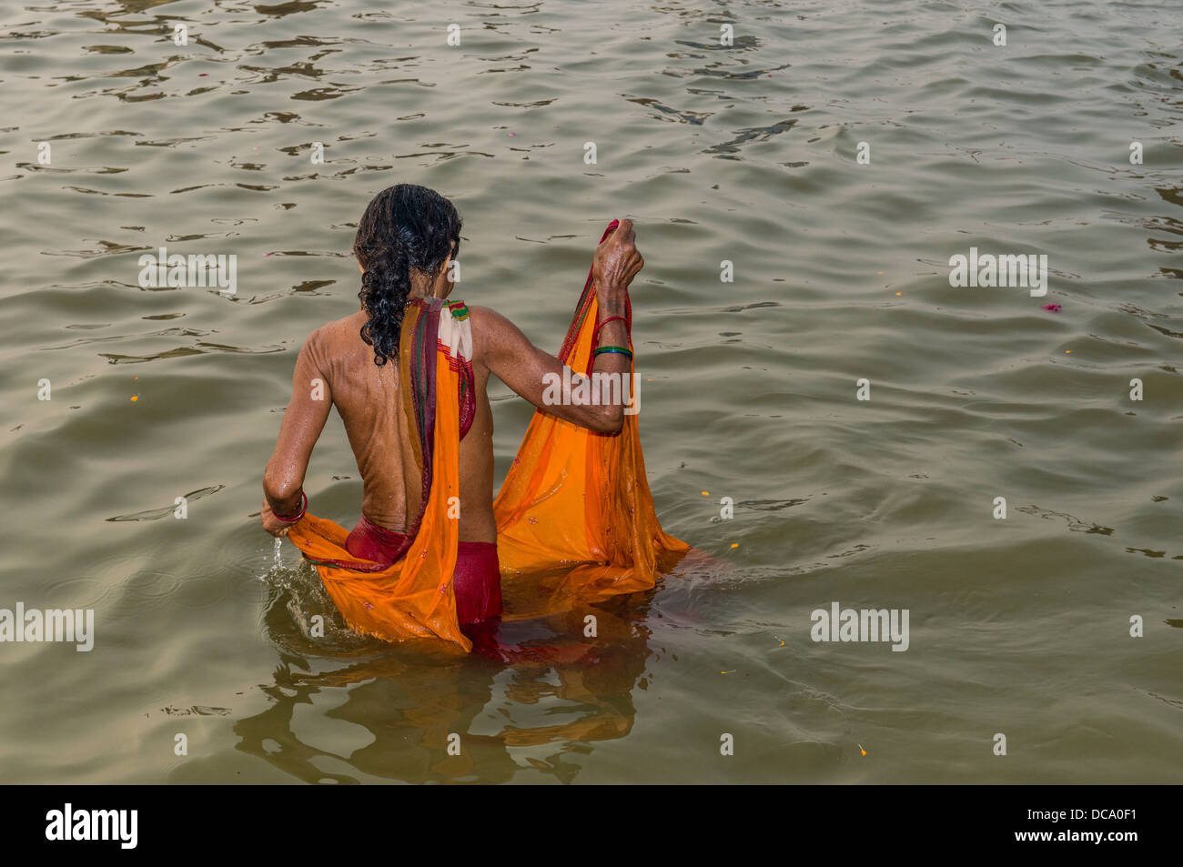 Mujer vistiendo un sari naranja tomar un baño en el Sangam, la confluencia de los ríos Ganges, Yamuna y Saraswati, en el Foto de stock
