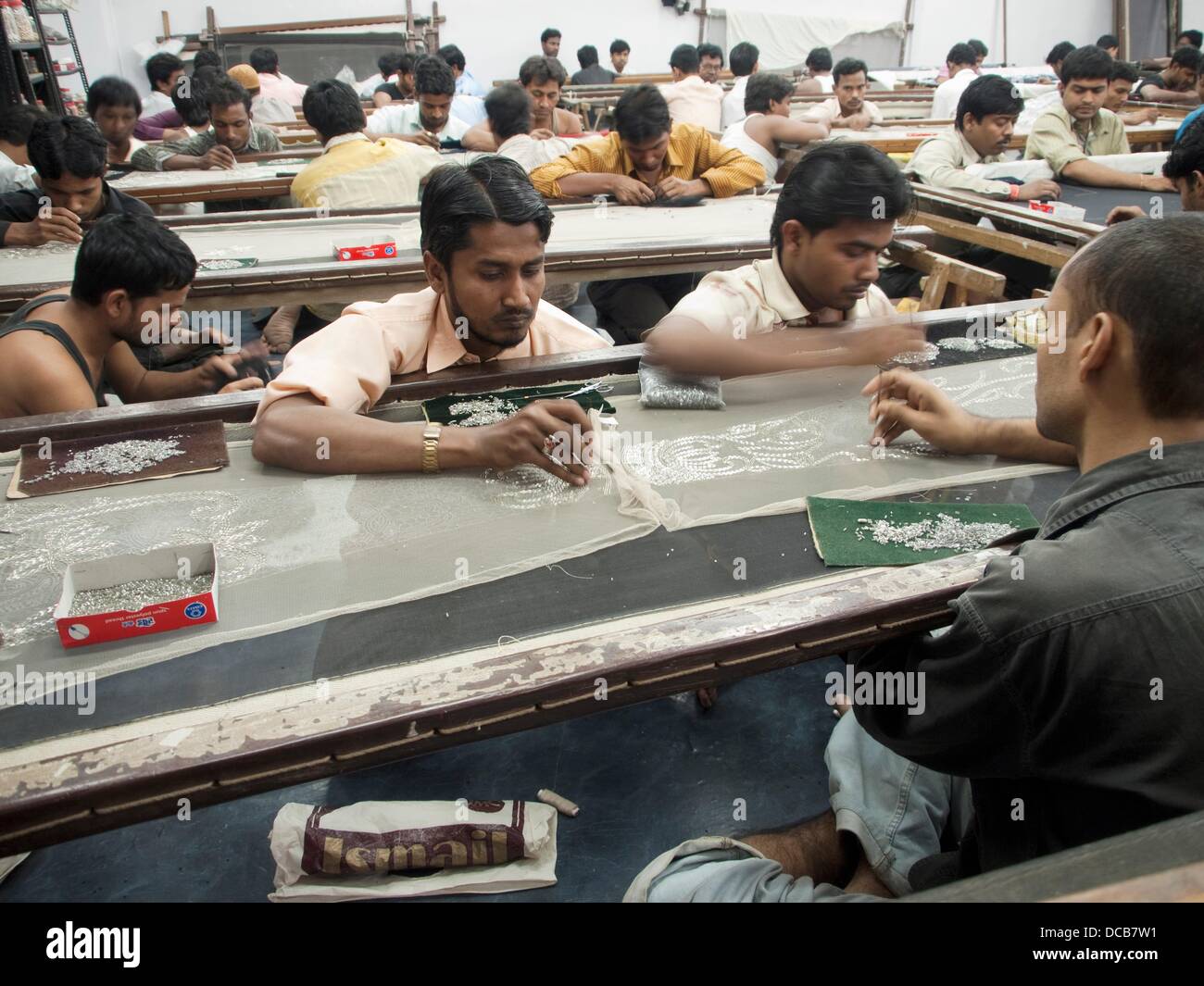 Los trabajadores colocar y coser cordones y adornos en tela en la Mumbai, India taller/oficina de una empresa de la India que hace Foto de stock
